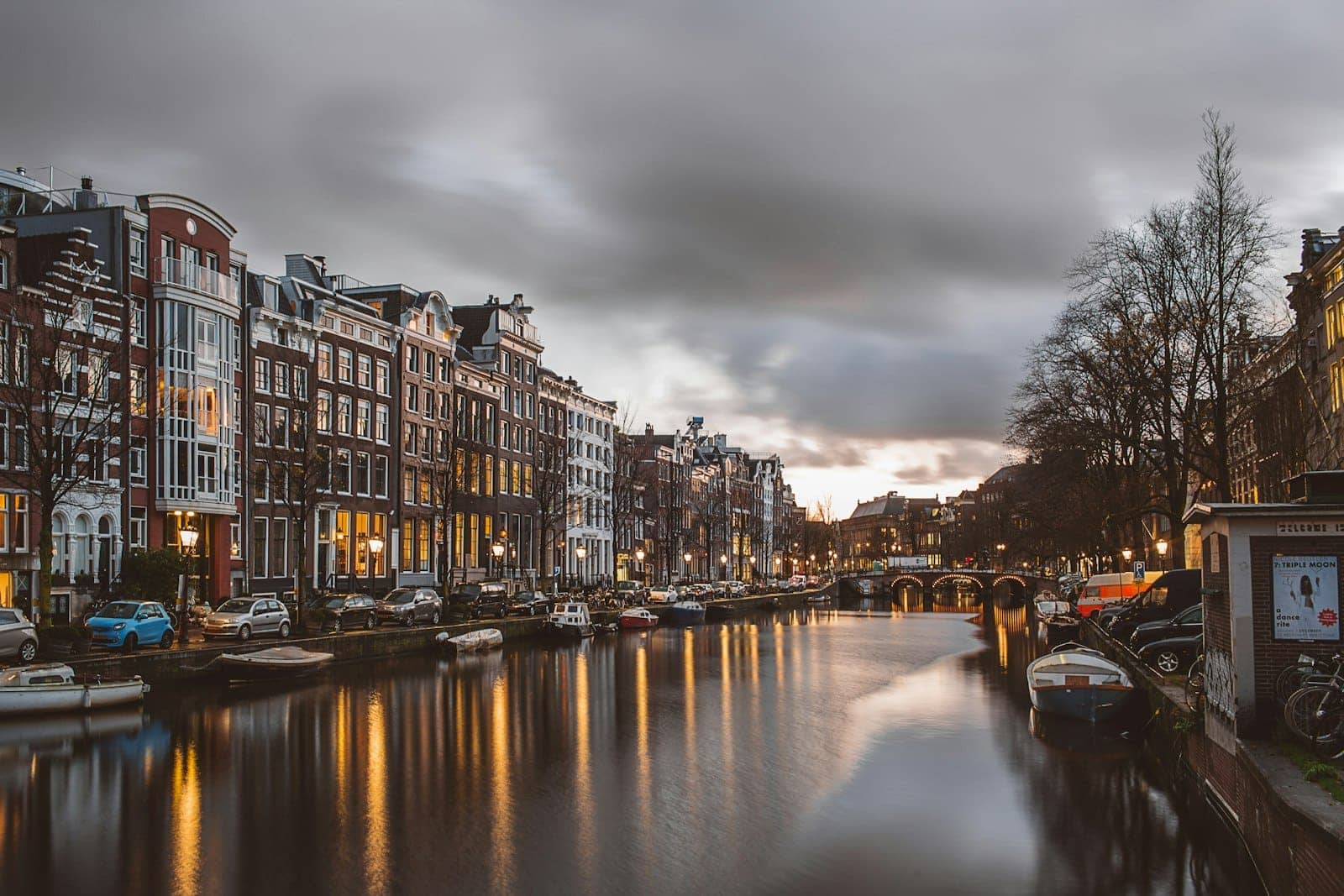 An Amsterdam canal at dusk with lit houses reflected in the water
