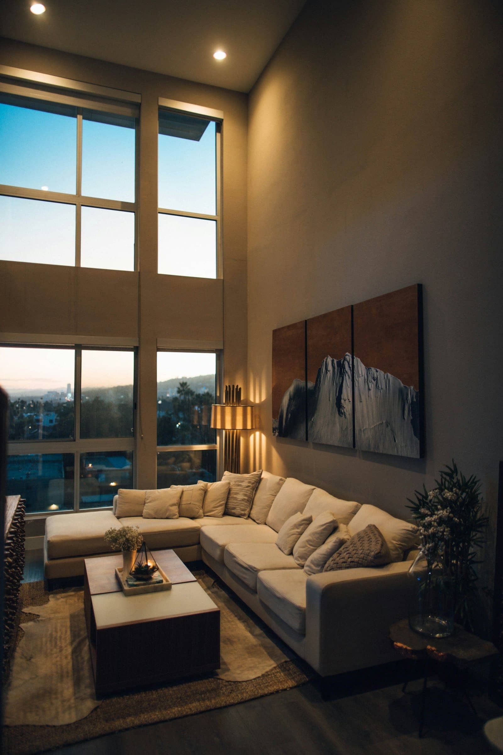 A dark living room with a large window and warm lamps